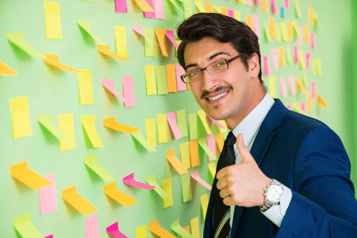 man giving a thumbs up in front of a wall of post it notes